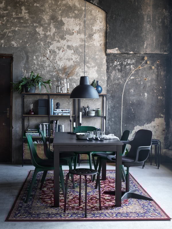 A dining area formed by a brown LANEBERG table and various chairs and stools, all standing on a multicolor VEDBÄK rug.