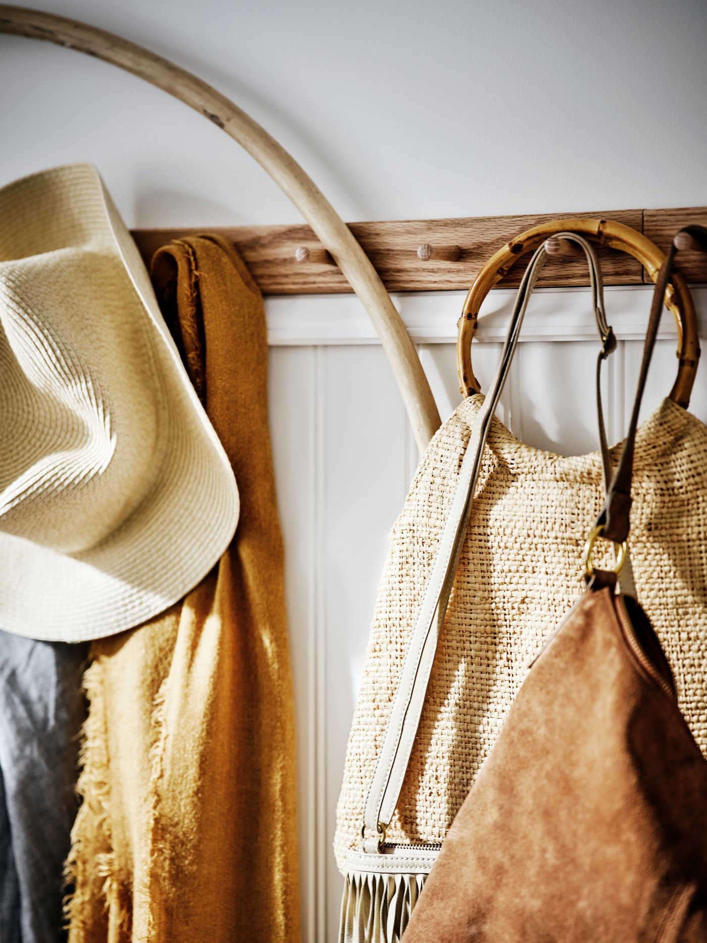 An oak HÖVOLM rack with six knobs on a white wood-panelled wall holding bags, hats and scarves.