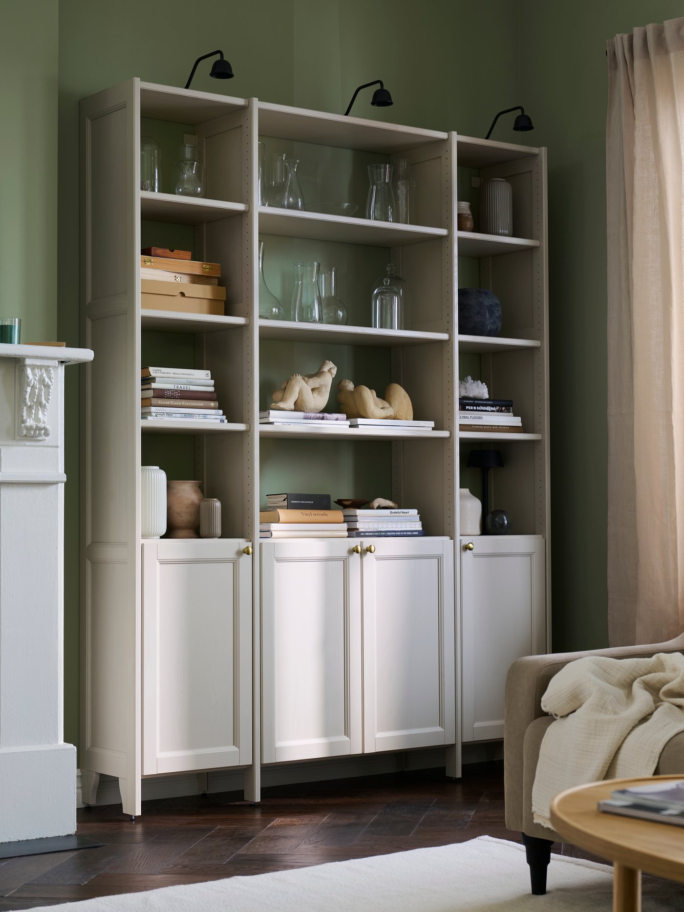 GULDDRAGARE storage system in a living room with a green wall and shelves with vases and books.