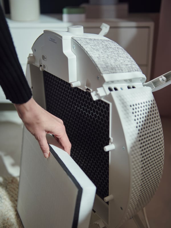 Lady using one hand to remove and replace white STARKVIND air purifier filter piece from air purifier.