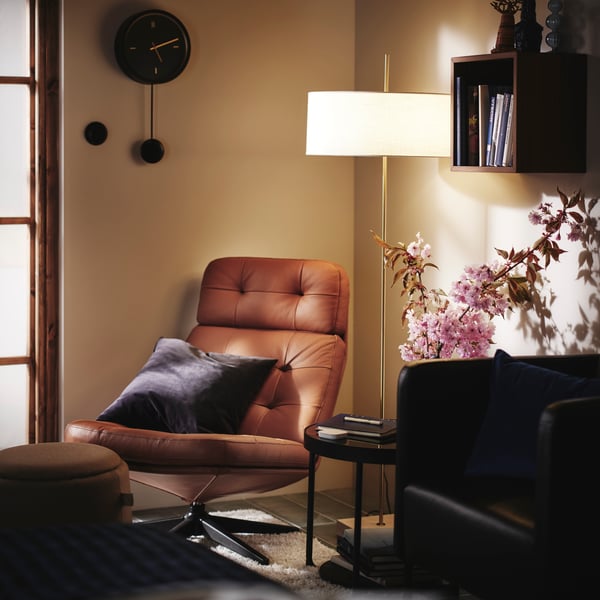 Relaxing corner in a bedroom with HAVBERG and EKERÖ armchairs, a side table, flowers, a floor lamp and a wall clock.