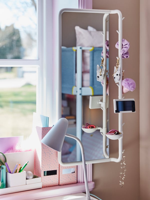 A MÖJLIGHET mirror holding a mobile phone and other small things, and a FUBBLA LED work lamp stand near a window.