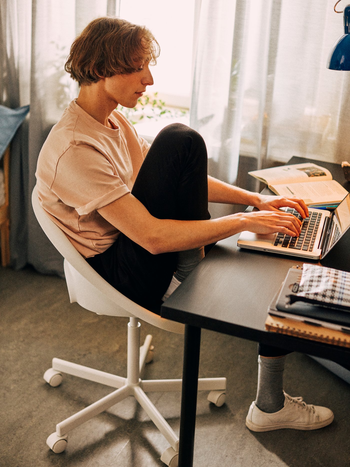 Un chico sentado en una silla giratoria LOBERGET/BLYSKÄR blanca escribiendo en un portátil colocado sobre una mesa LINNMON/ADILS.