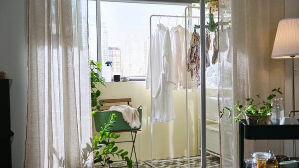 A JOSTEIN shelving unit with drying rack that has clothes on it in an enclosed balcony is seen through an open sliding door.