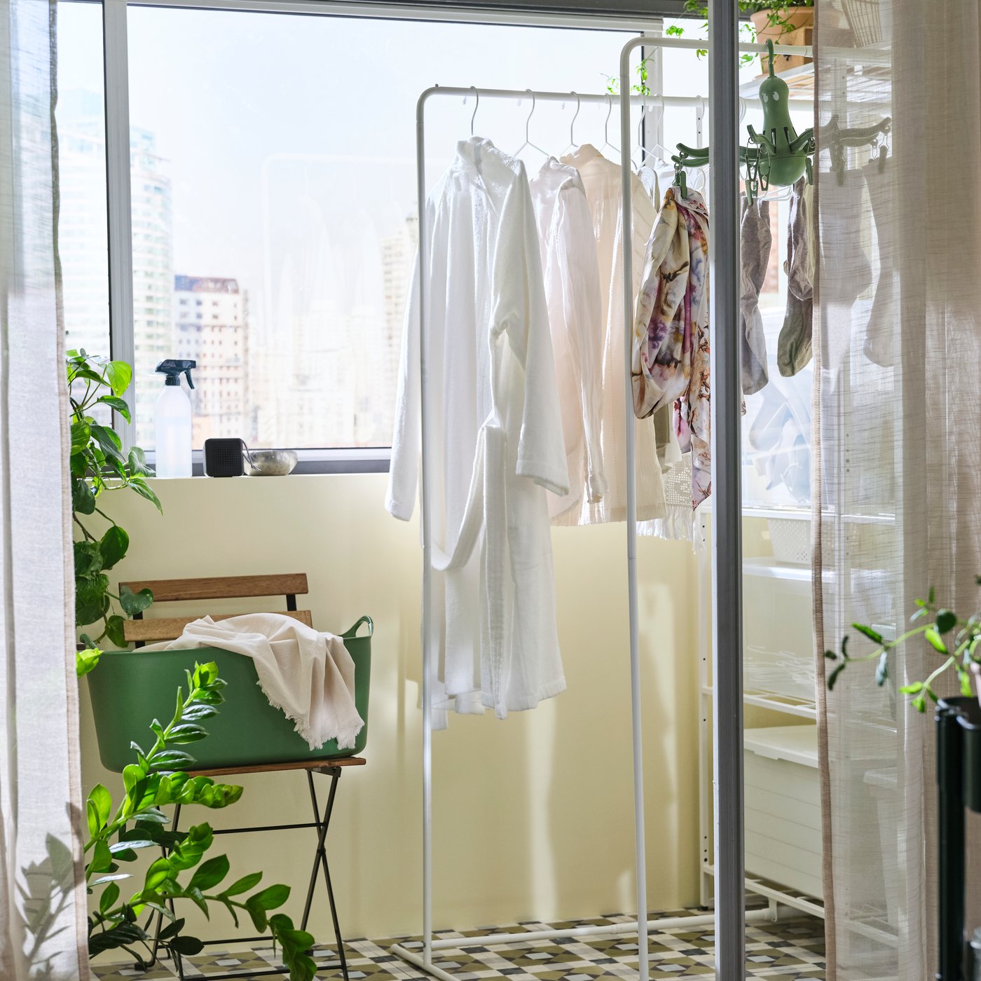 A JOSTEIN shelving unit with drying rack that has clothes on it in an enclosed balcony is seen through an open sliding door.