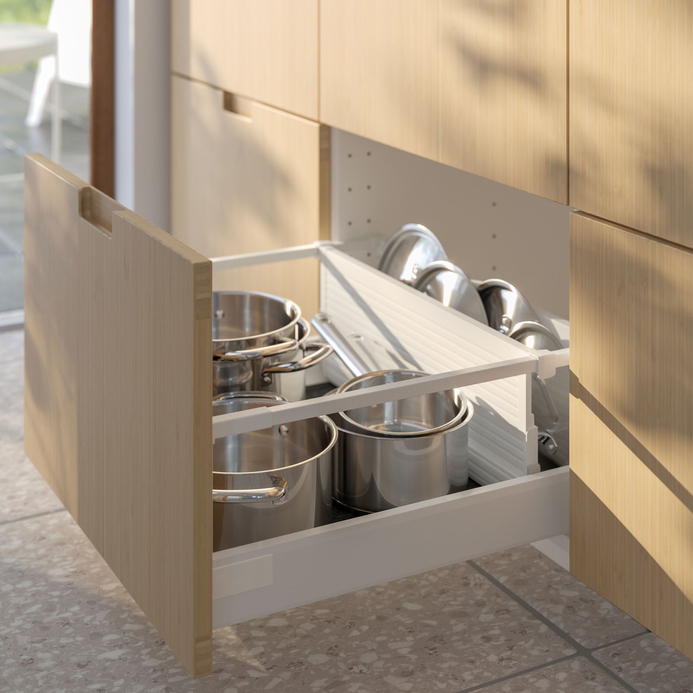 En un cajón de cocina abierto, un separador UPPDATERA para cajones separa las ollas y sartenes IKEA 365+ de sus tapas.