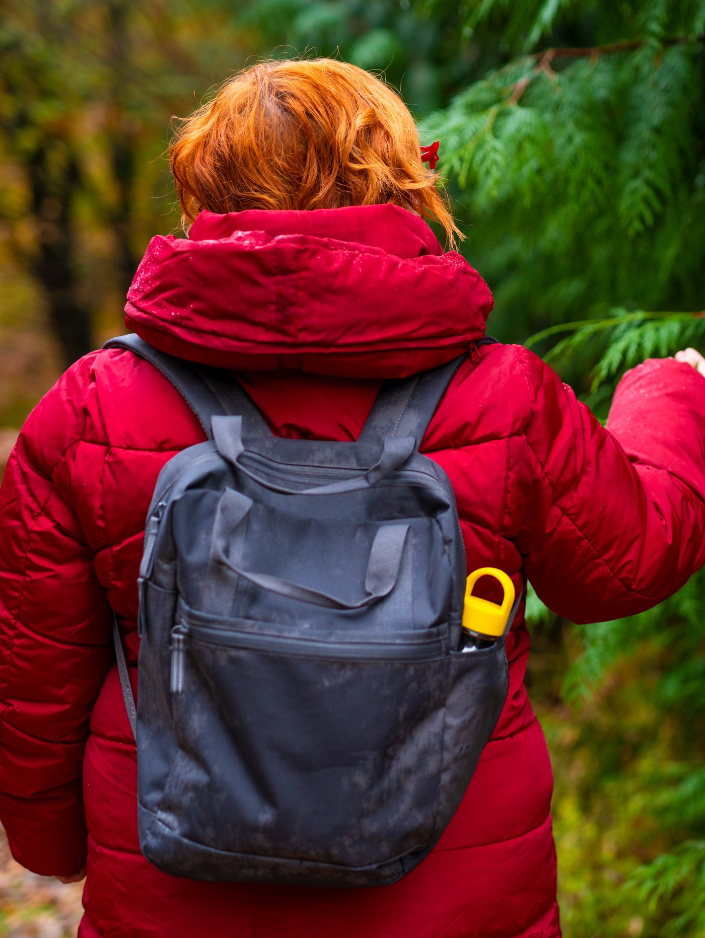 A woman in a forest is gently touching a pine tree with her hand. She is carrying a STARTTID backpack with a FORMSKÖN water bottle i it.