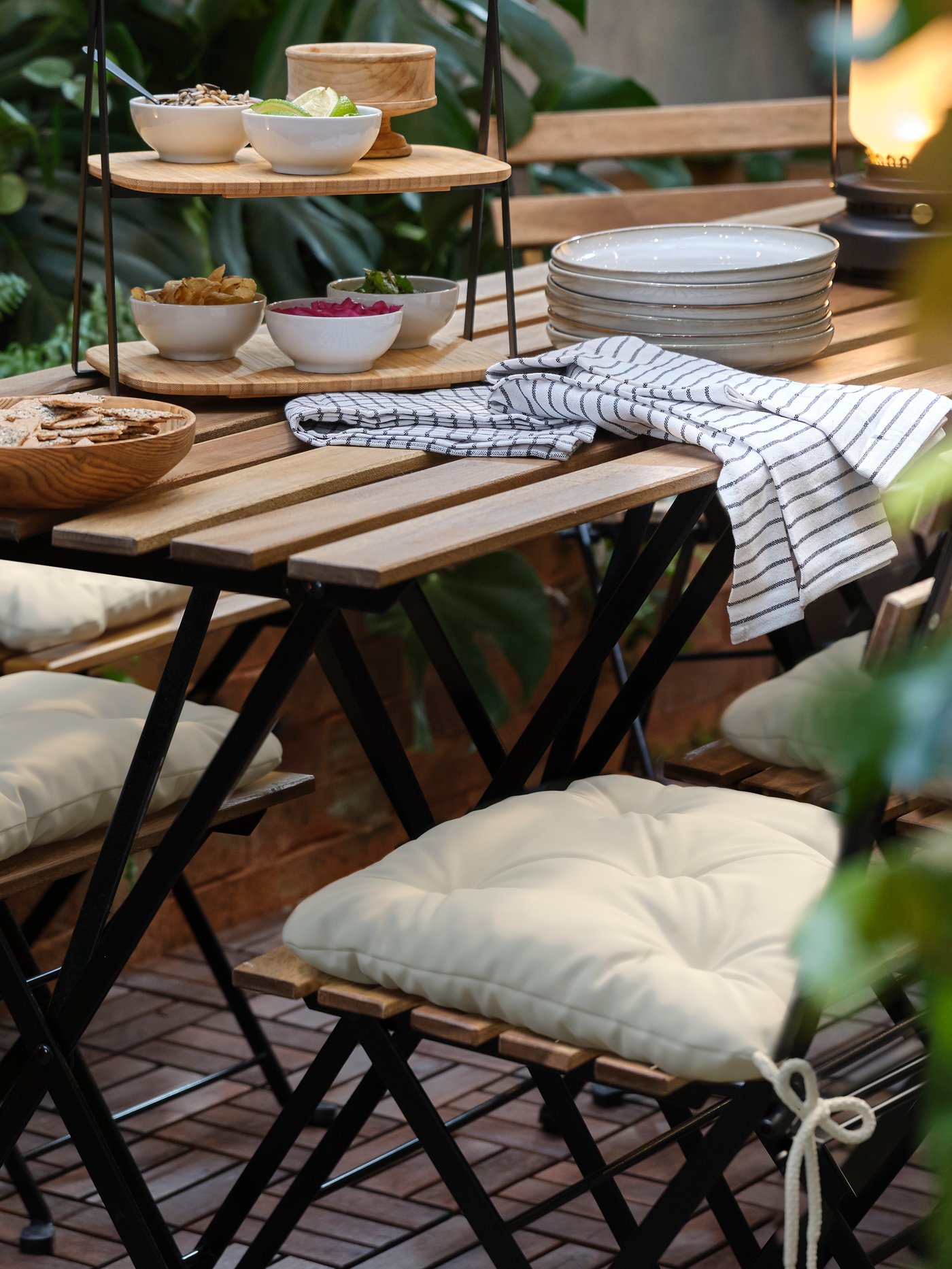 Zona exterior con un cojín beige encima de una silla. La silla se encuentra sobre una mesa cuadrada sobre la que hay una bandeja para servir.