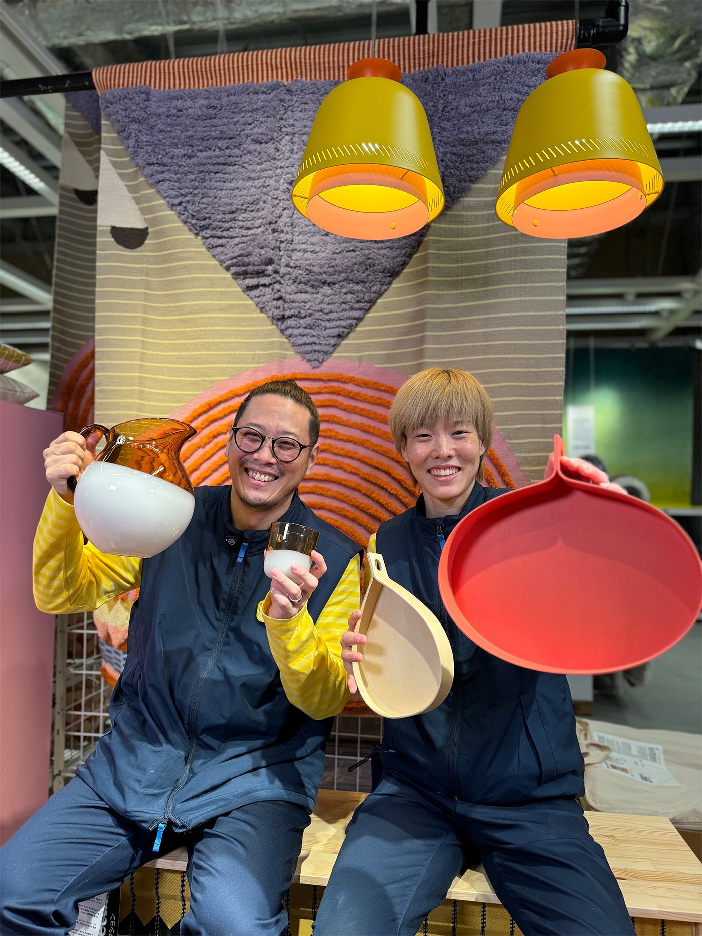 イケアのコワーカーがカラフルなキッチン雑貨を手に笑顔で座る、ショールームの楽しい売場シーン