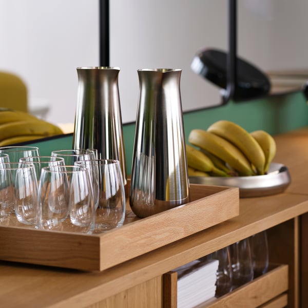 A wooden tray with glasses on it and 2 stainless steel jugs.