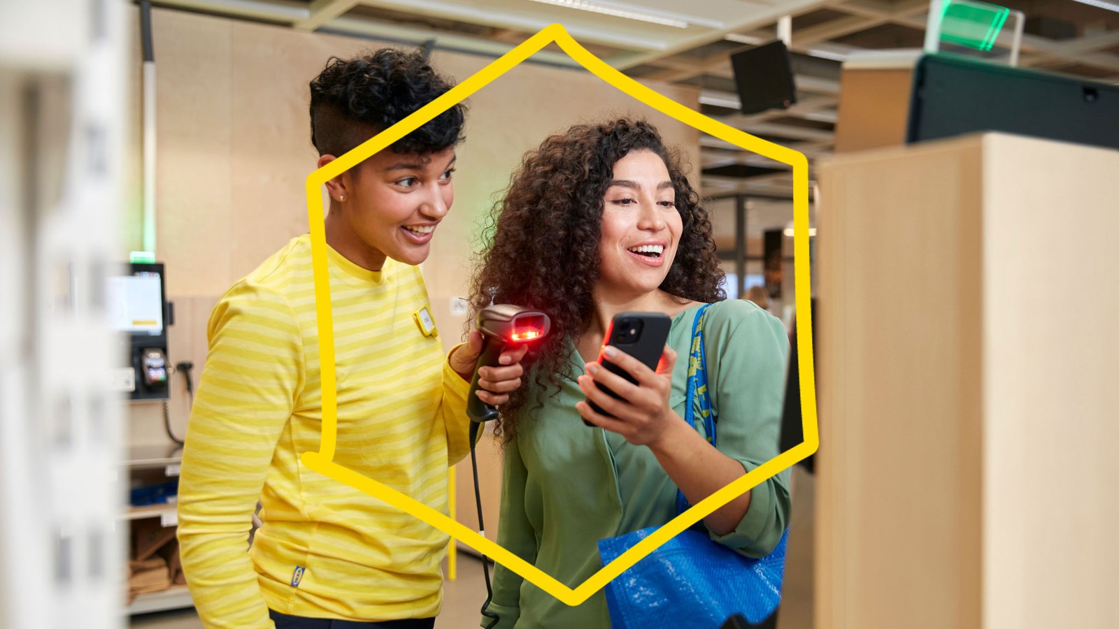 An IKEA co‑worker is helping a customer at the checkout by scanning something on the customer’s phone.