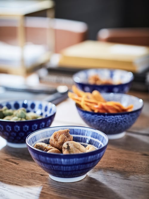 Snacks in vier gemusterten ENTUSIASM Schüsseln in Blau auf einer Holzoberfläche.