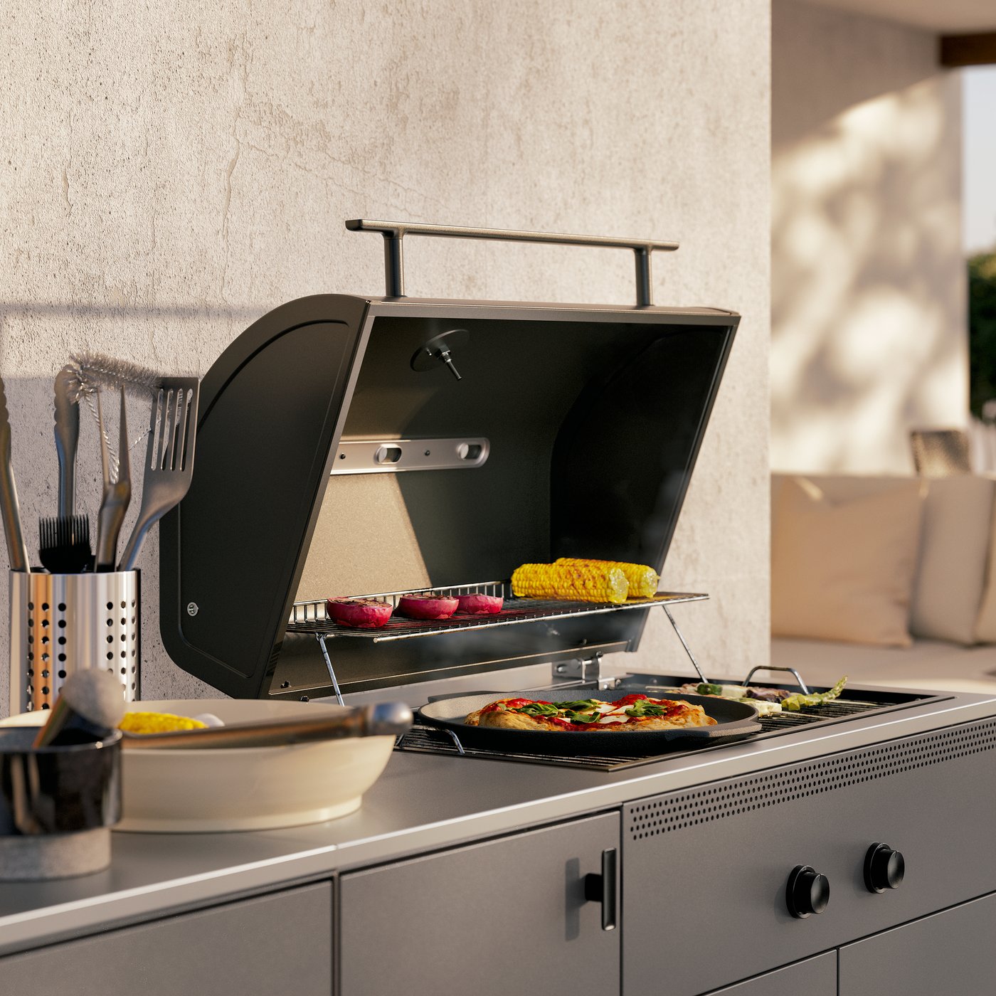 A close-up of the barbecue part of a dark grey BÅTSKÄR outdoor kitchen. The lid is open, showing a pizza and vegetables.