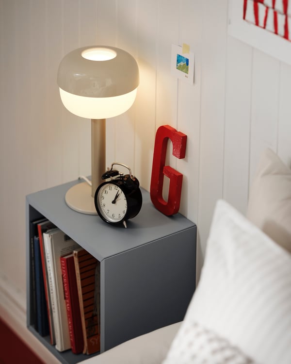 A DEKAD alarm clock atop an EKET cabinet that’s otherwise filled with tableware and wall-mounted next to a VITVAL loft bed.