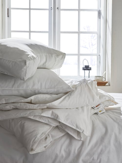 FJÄLLARNIKA double duvet and pillows on a white bed with a white wall and window in the background.