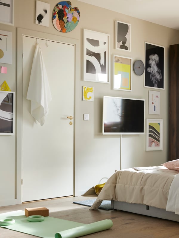 A variety of BILD posters in white frames and a TV on a beige wall in front of a bed with a HEDFRYLE comforter on it.