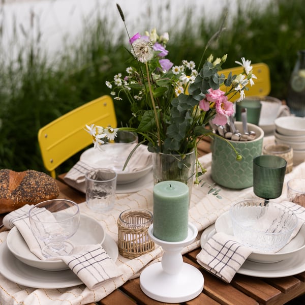 A midsummer table setting with green block candles and yellow chairs.