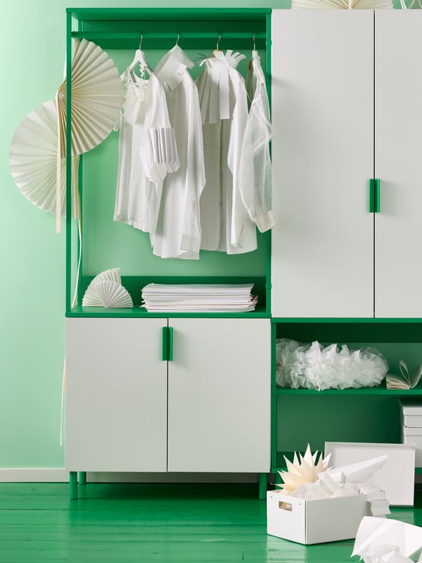 Ein grüner Raum mit einem grünen offenen Kleiderschrank mit weißen FONNES Türen. Im offenen Teil hängen weiße Hemden und stehen weiße Boxen.