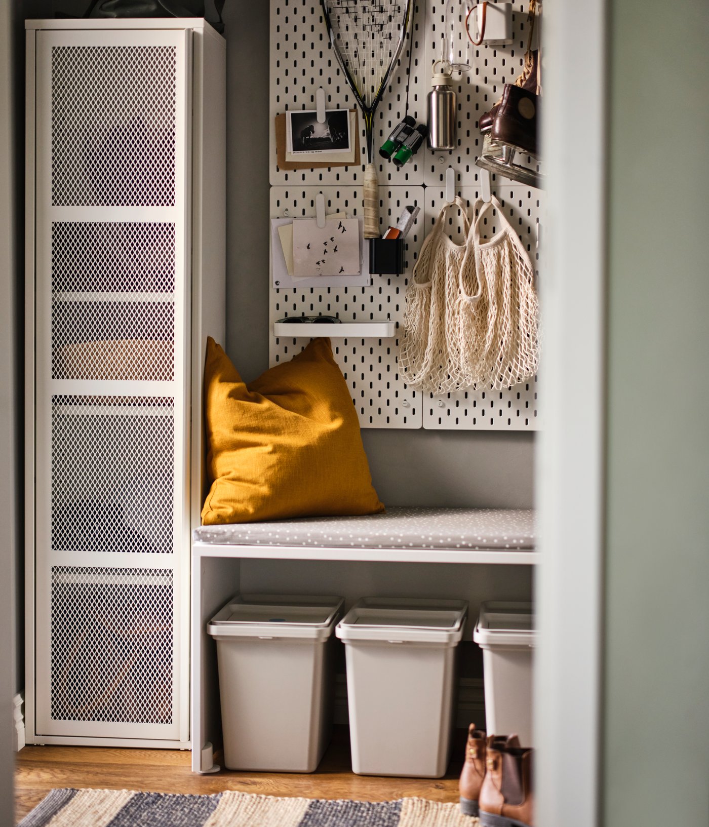 A white mesh IVAR cabinet next to a bench with a SKÅDIS pegboard above and three light grey HÅLLBAR bins with lids below.