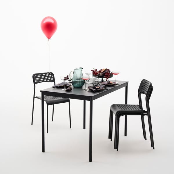 A black SANDSBERG dining table is set for four people with dinnerware and fruit. Next to the table, four chairs.