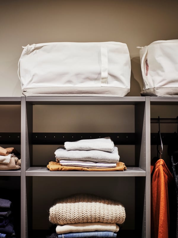 A LACKISAR storage case sits on top of an open AURDAL wardrobe, with folded clothes lying on the shelves below.