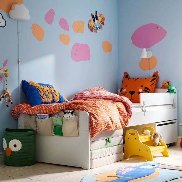 In una cameretta con tanti colori, un letto SLÄKT lungo una parete azzurra su cui sono dipinte delle macchie rosa e arancioni.