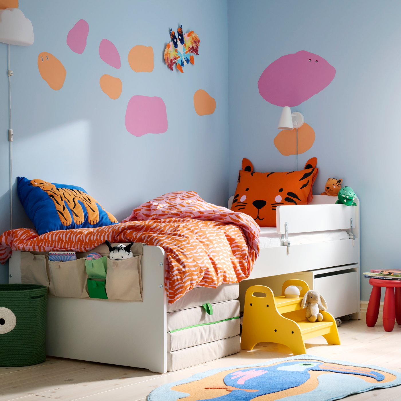 Quarto de criança colorido, cama SLÄKT encostada a parede azul pintada com formas rosa e laranja.