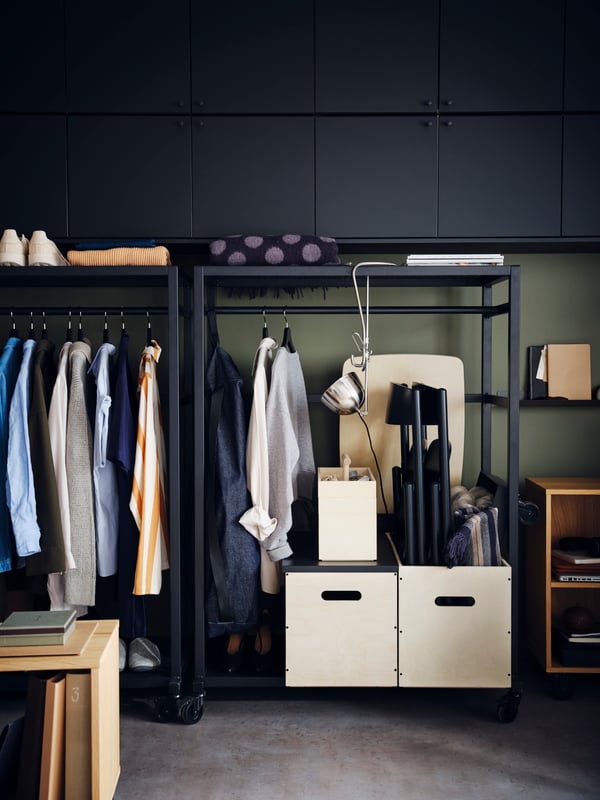 Black RÅVAROR storage units on casters are filled with clothing and RÅVAROR boxes, with a RÅVAROR throw lying on top.