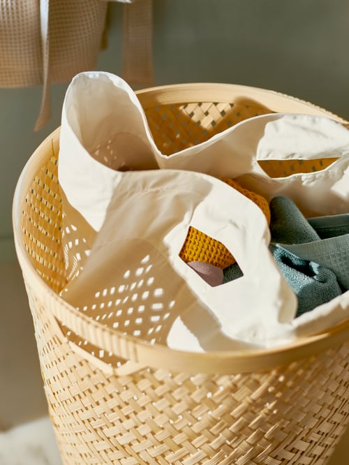 The inner bag peeks out of a handmade SALUDING bamboo laundry basket in a sunlit setting.
