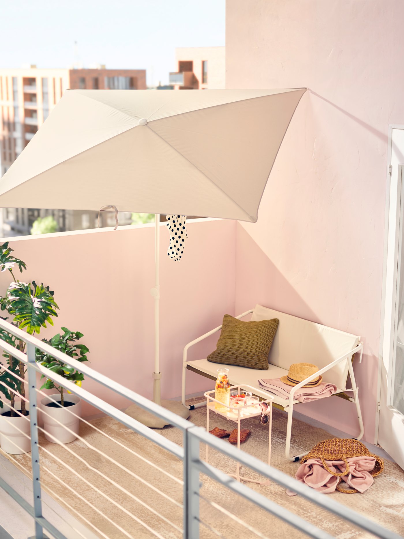 Una sombrilla TVETÖ blanca ayuda a crear un cómodo lugar de descanso en este balcón urbano con muebles de exterior blancos y paredes de color rosa.