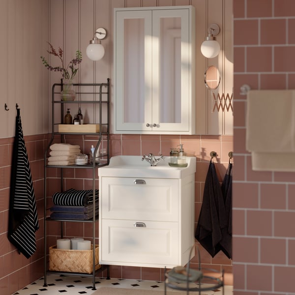A bathroom with a white TÄNNFORSEN vanity unit, featuring two drawers and a washbasin, next to a metal shelf with towels.