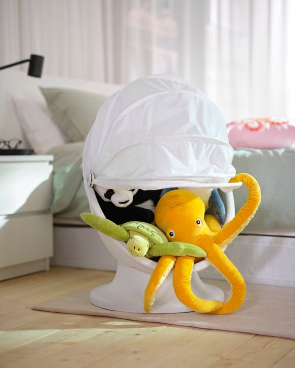 En gul BLÅVINGAD bläckfisk-mjukisdjur ligger i en vit IKEA PS LÖMSK fåtölj i ett sovrum.