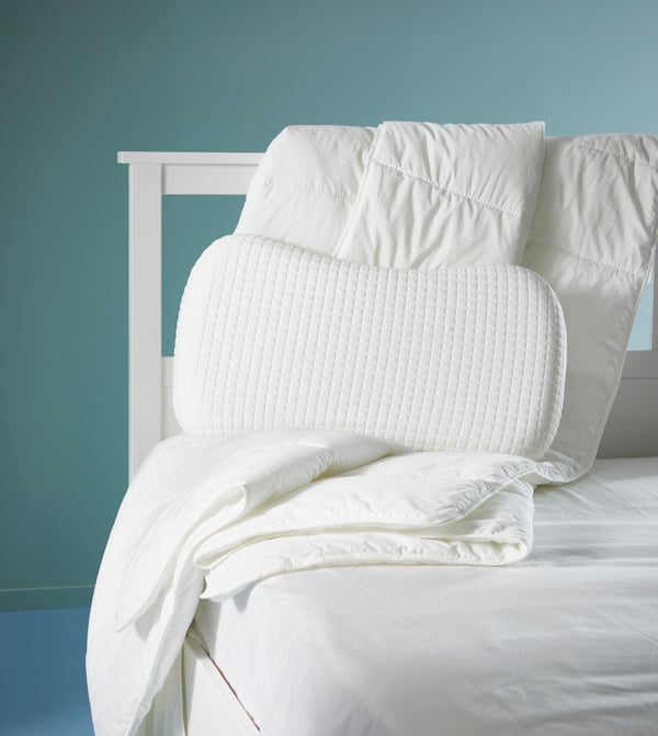Ein weißes Bett mit Decke und Kissen steht in einem türkisfarbenem Raum.