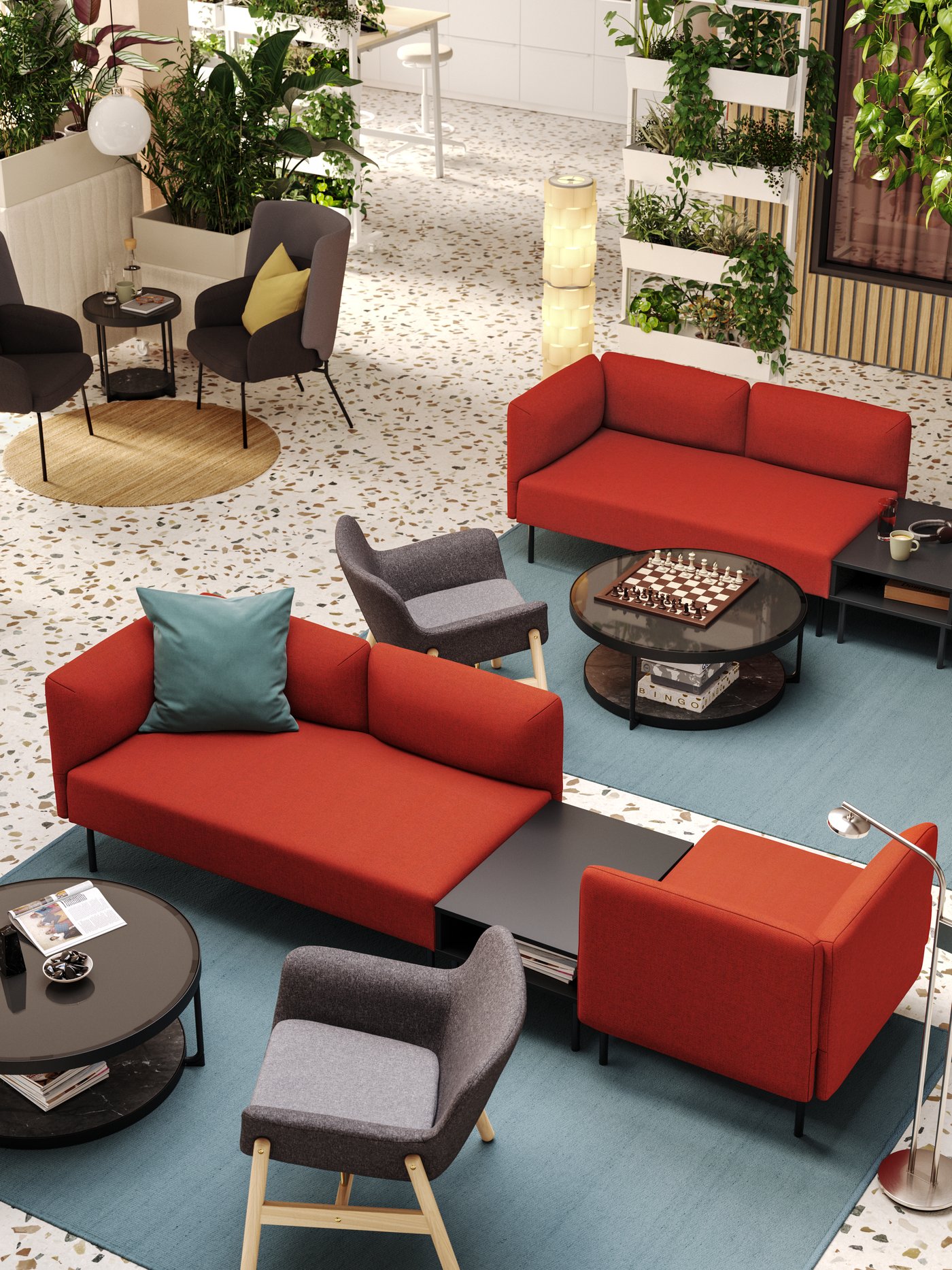 An aerial view of a hotel lobby with two seating areas defined by red LILLEHEM modular sofas and grey armchairs on big rugs.