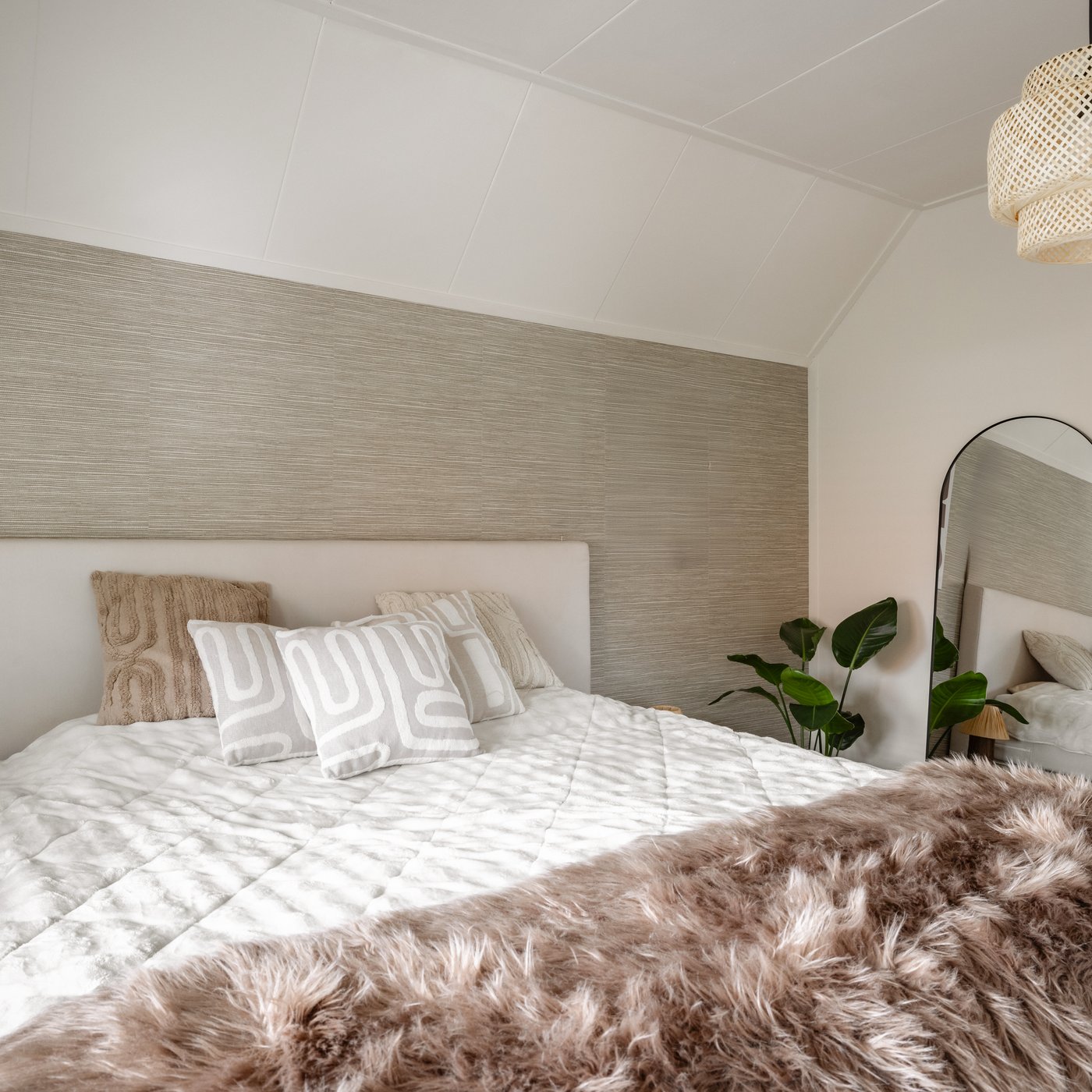 Slaapkamer met wit tweepersoonsbed. Tegen de muur leunt een zwarte LINDBYN spiegel. Boven het bed hangt een SINNERLIG hanglamp.