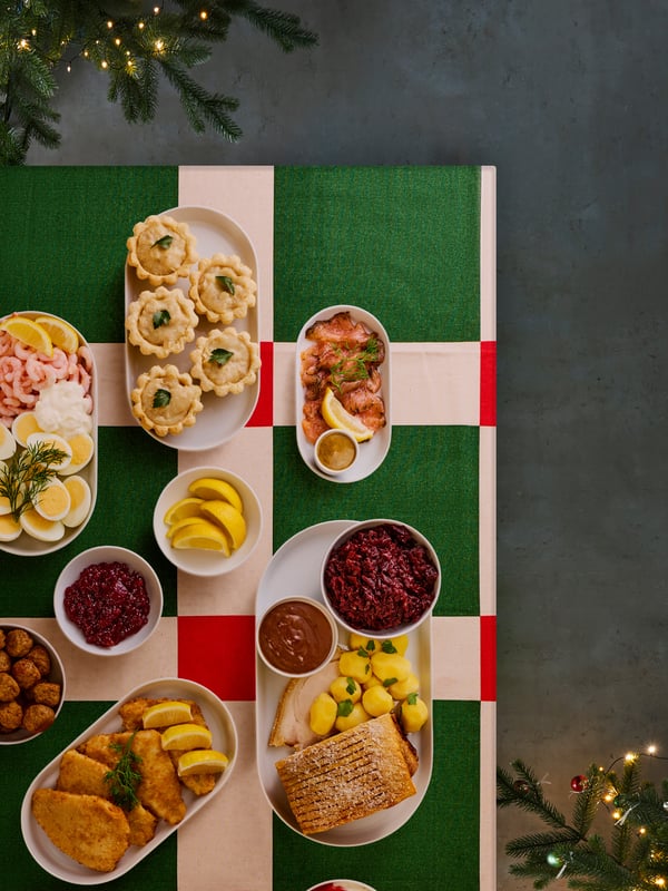 Oversigtsbillede af et julebord dækket med en VINTERFINT dug i røde og grønne tern. På bordet står en masse juleretter på hver deres tallerken.