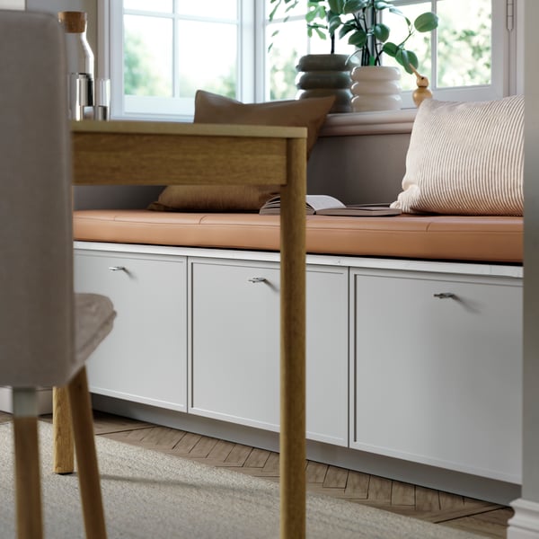 Banquette avec façades de tiroirs ASPUDDEN en gris clair en dessous, recouverte d'une assise en cuir et de coussins décoratifs.
