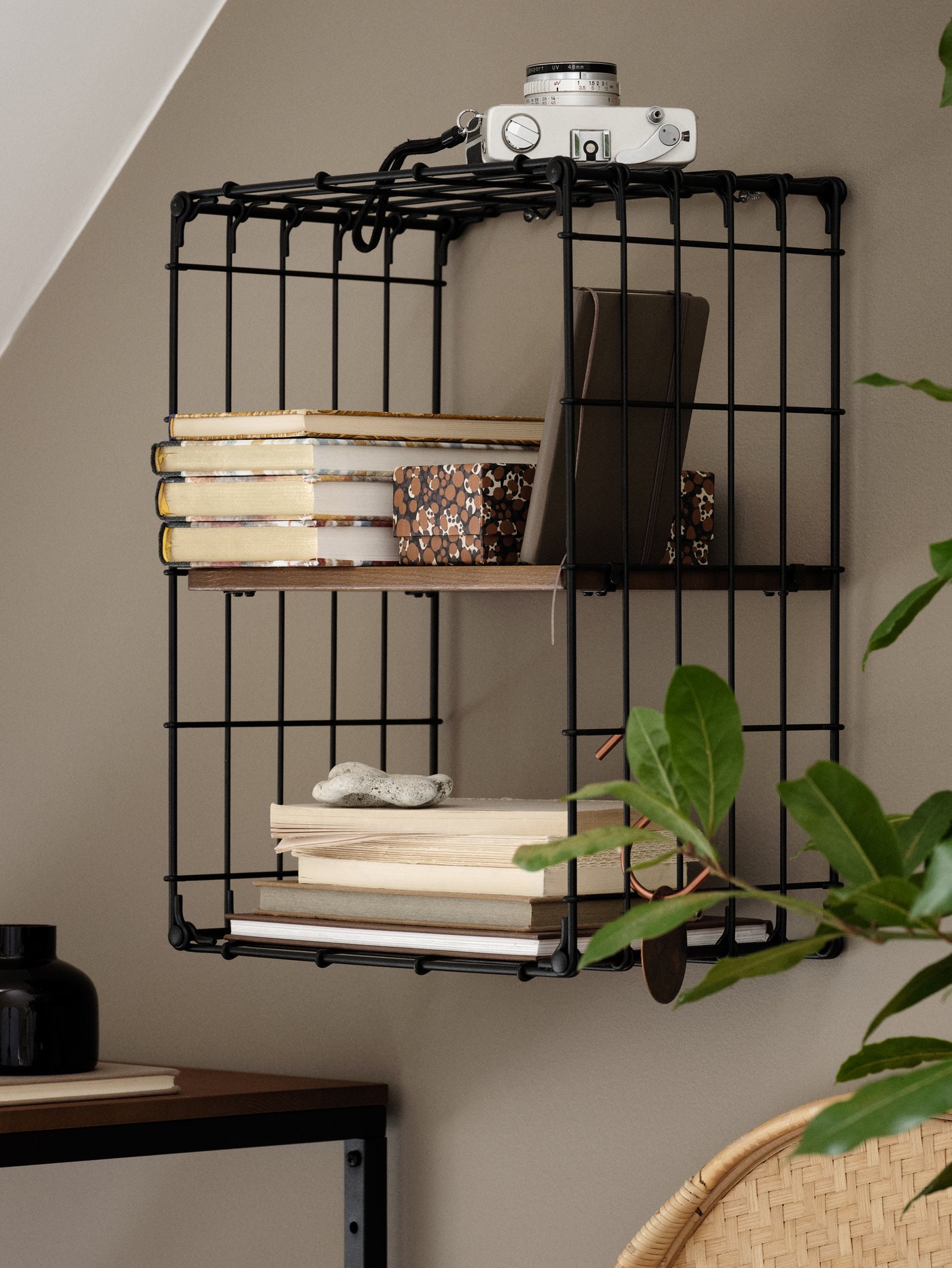 Estante de pared de madera de pino de color negro de estilo clásico con libros, una cámara, una caja y una piedra.