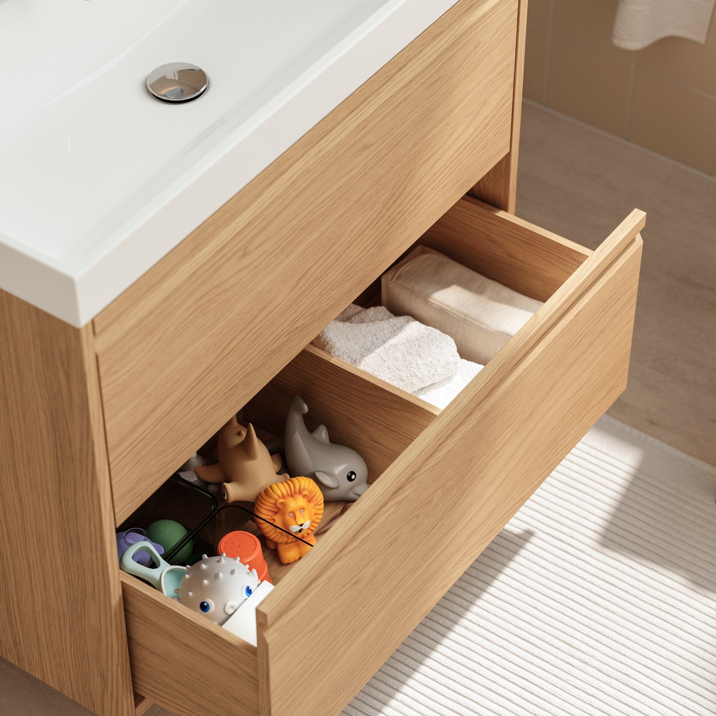 An oak effect ÄNGSJÖN/BACKSJÖN vanity unit has its bottom drawer open, showing white towels and bath toys in boxes.