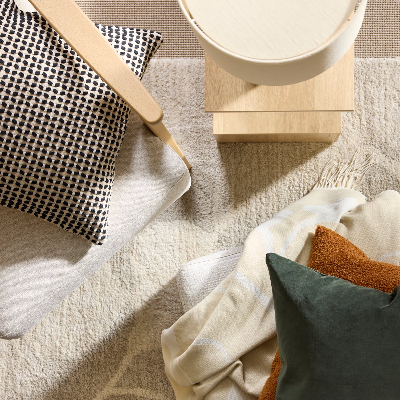 Cushions and a throw on a light-beige EKENÄSET high-back armchair and footstool standing on an ÄLSKEGRAS low-pile rug.