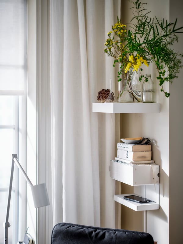 A white LACK shelf holding a vase with flowers in it is attached to a wall above a SYMFONISK speaker combination with shelf.