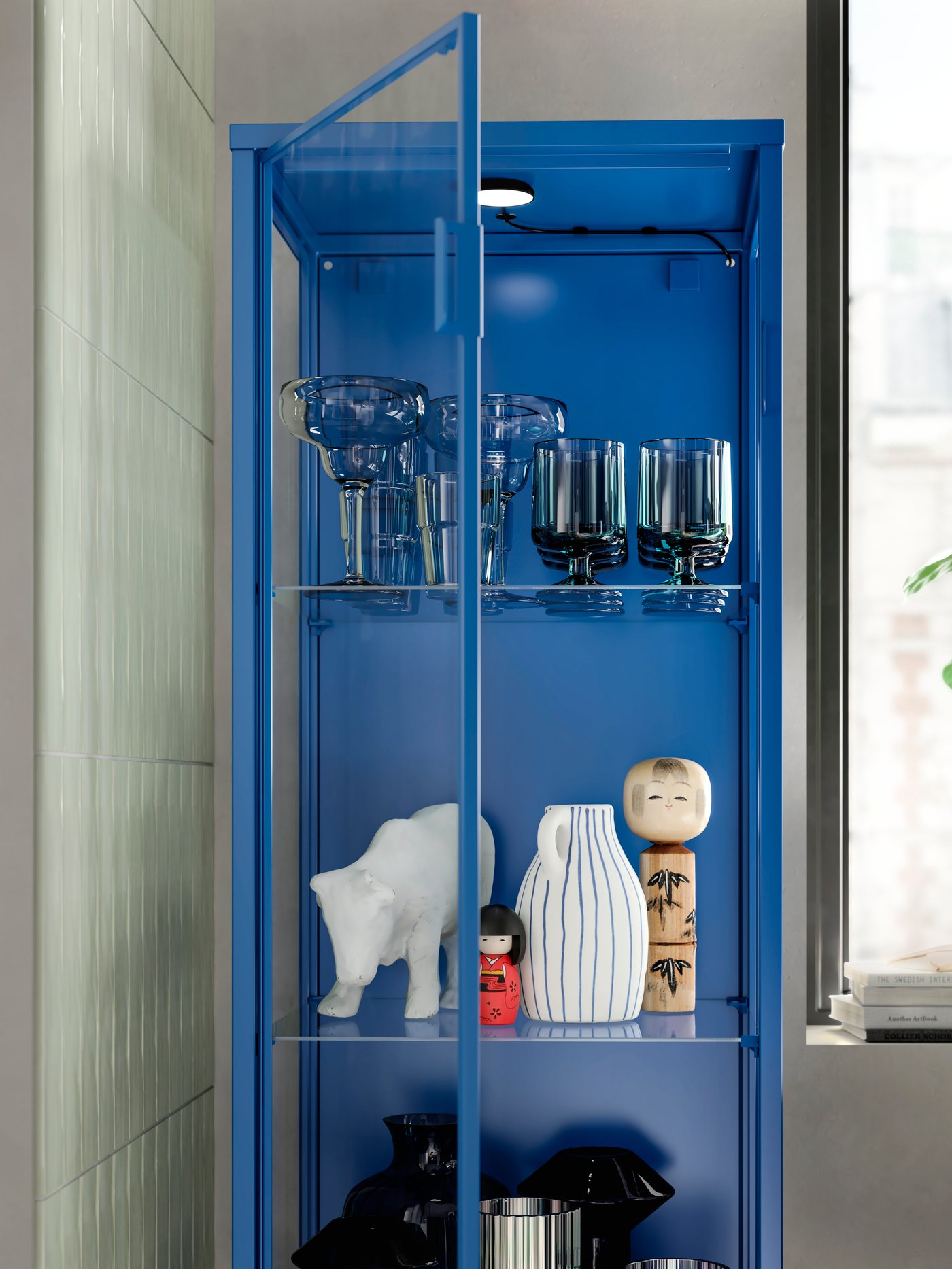 A blue RUDSTA glass cabinet next to a bright window in a living room.