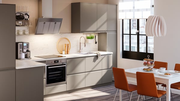 A luminous L-shape kitchen with UPPLÖV drawer fronts in matte dark beige, and EKBACKEN worktops in white marble effect laminate.