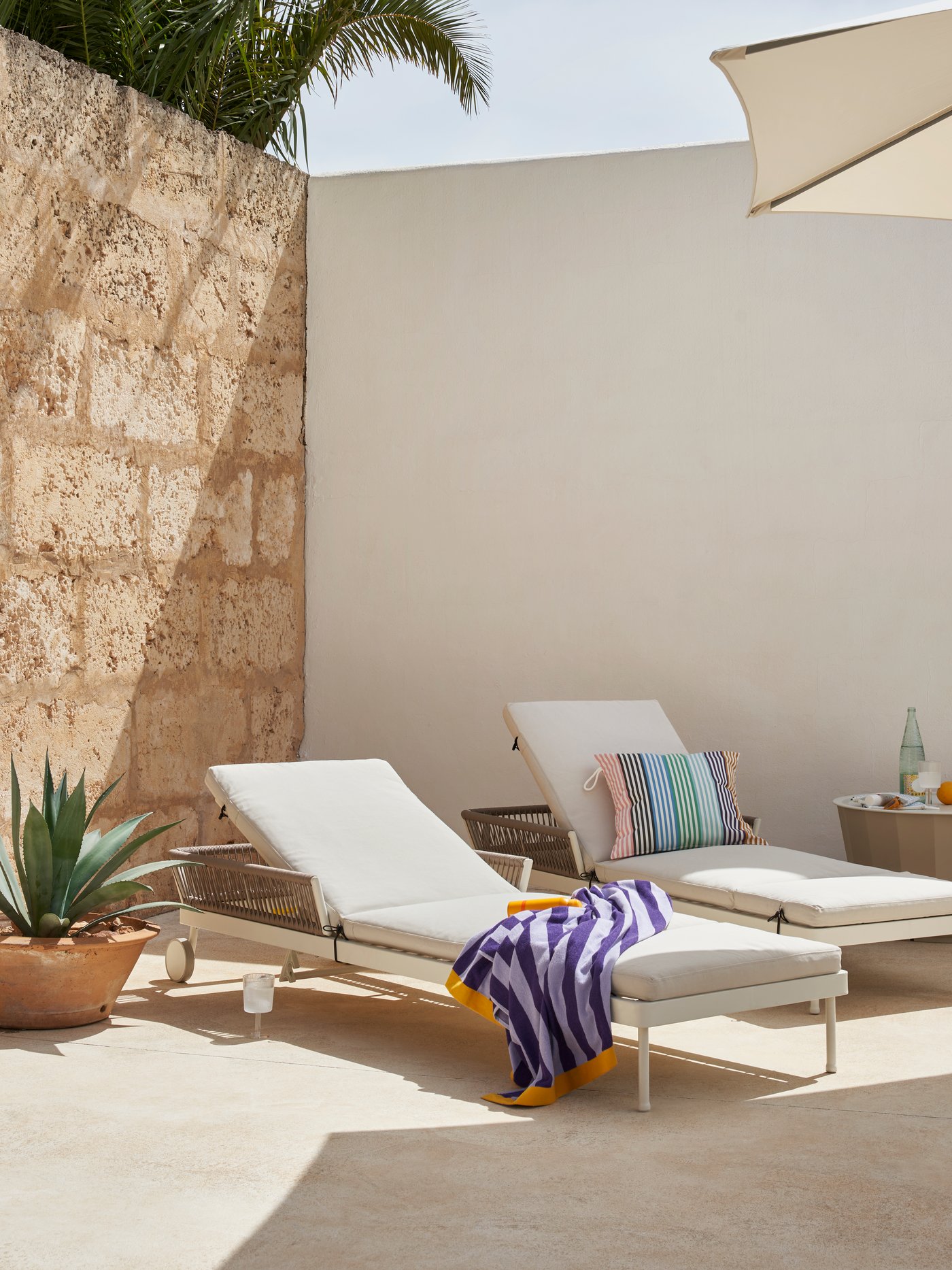 Exterior con varias tumbonas SEGERÖN colocadas junto a una sombrilla JOGGESÖ beige y una mesa de centro LÅGASKÄR.