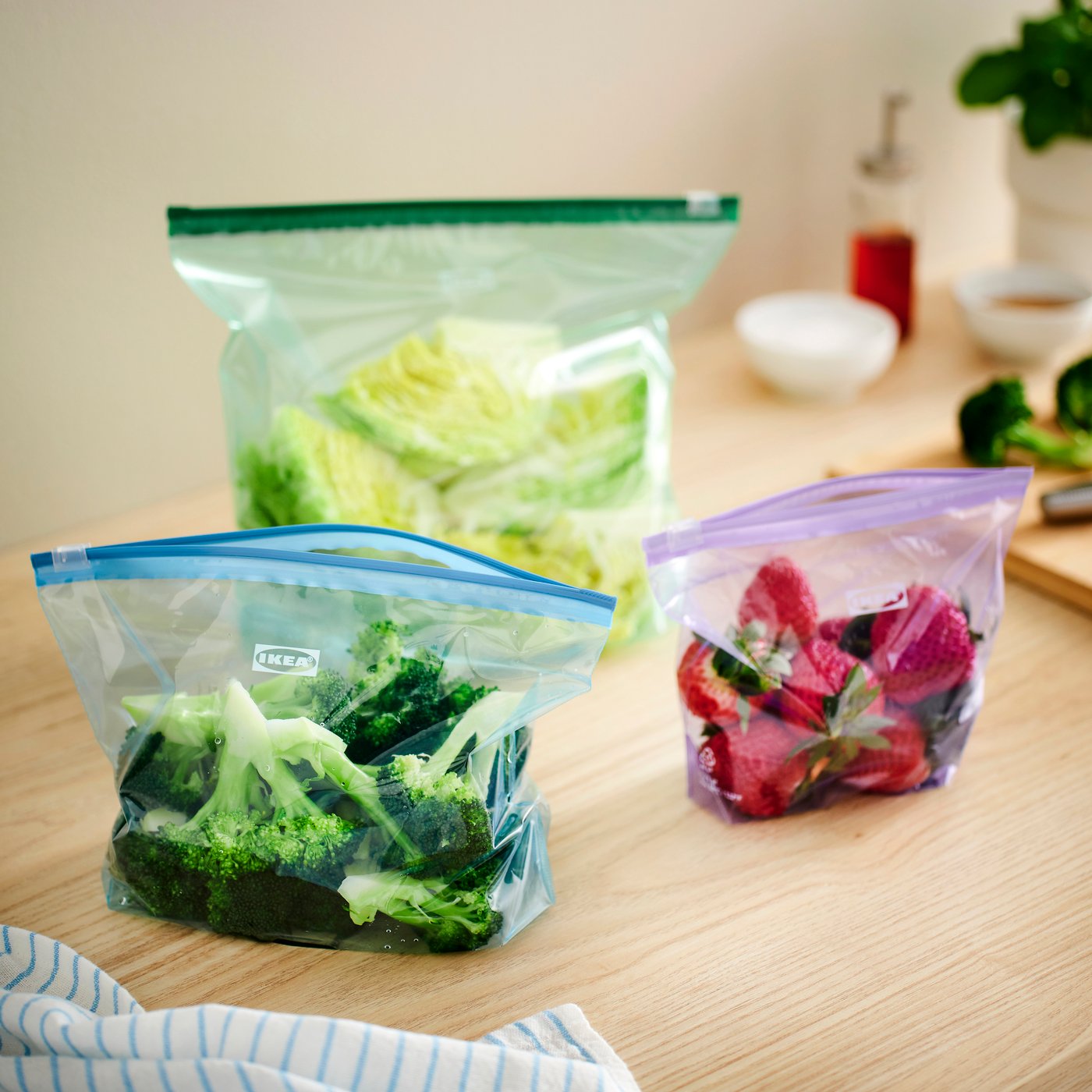 Многоразовые пакеты с застёжкой, наполненные свежими овощами, стоят на деревянной кухонной столешнице.