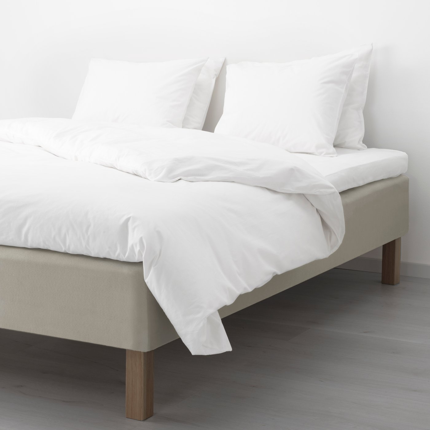 En boxmadras med ben er redt op med hvidt sengetøj på dyne og hovedpude. 