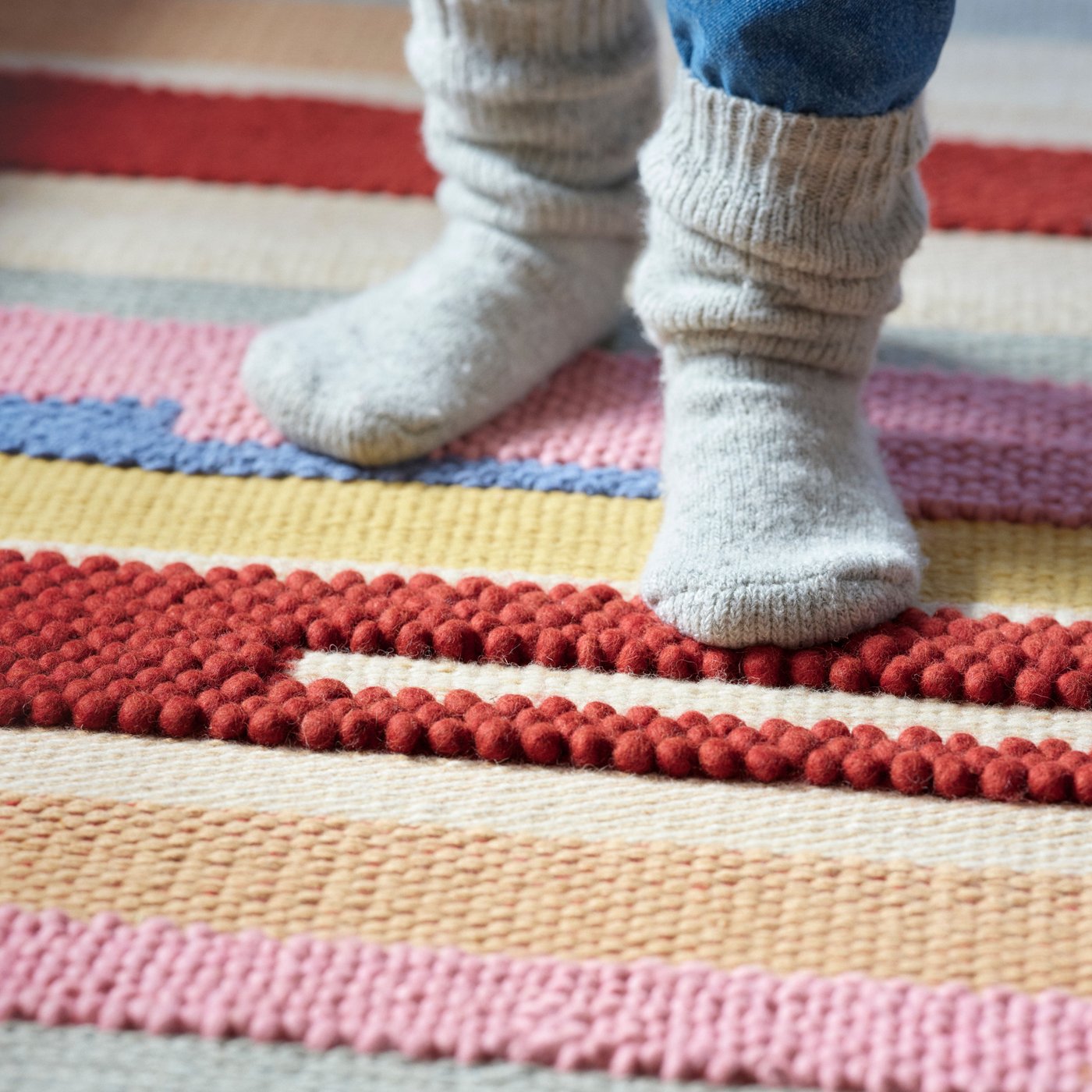 Monivärisellä raidallisella BRÖNDEN-matolla on jalat, joissa on villasukat.