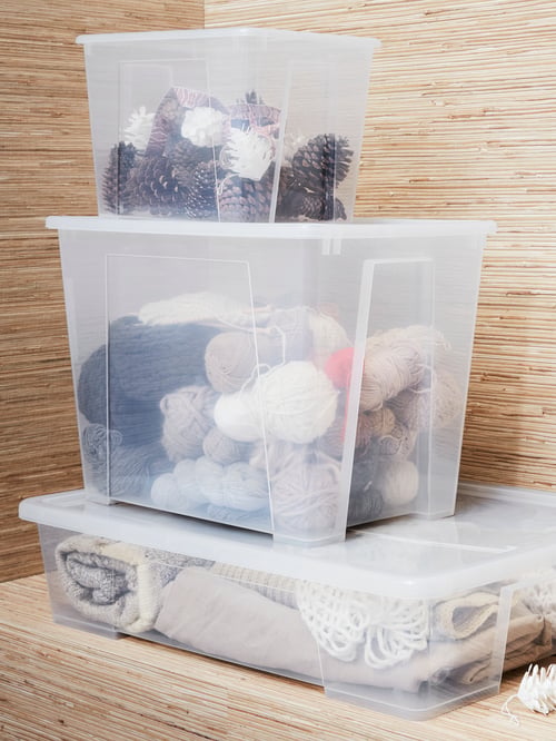Wooden cabinet with three transparent plastic storage bins of different sizes, one with clothes, one with balls of yarn.