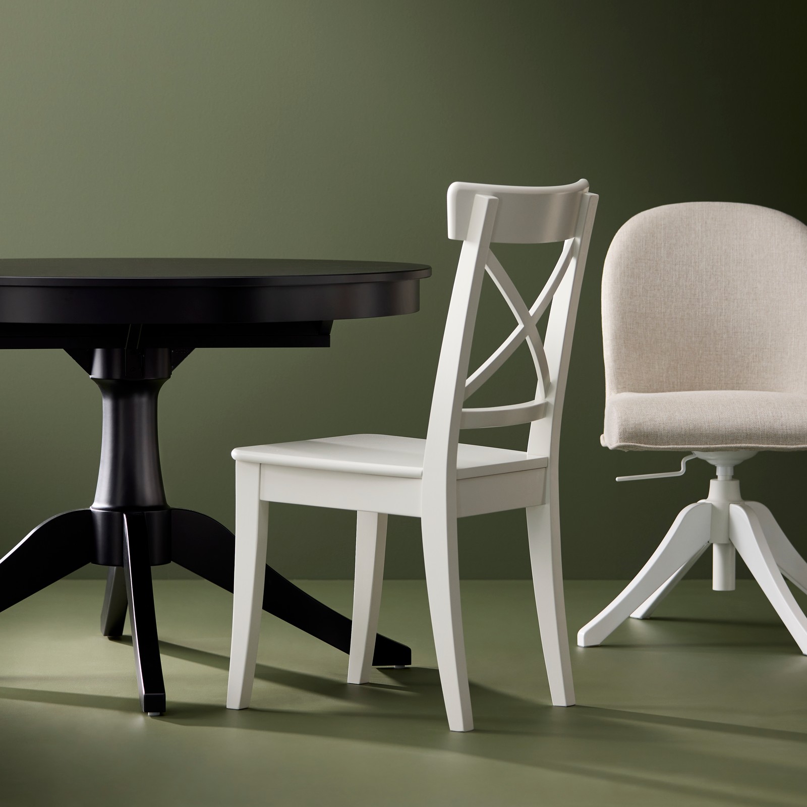 A black ROSENTORP extendable table, a white ROSENTORP chair and a swivel chair are placed against a green background.