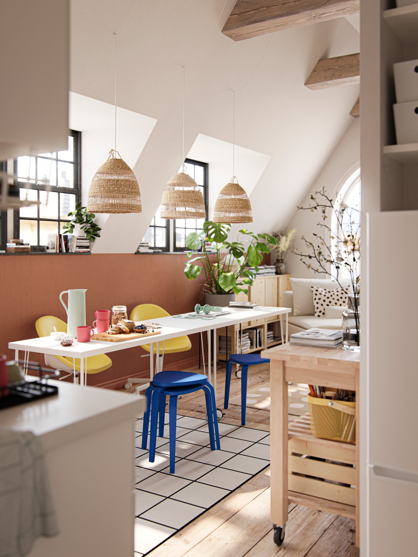 A sun-drenched dining area with two tables, blue stools, yellow chairs and three pendants made from natural materials.